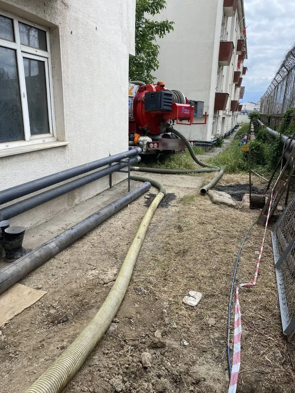 İki bina arasındaki dar geçitte kombine kanal açma aracı, hortumu açık rögara uzatılmış